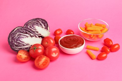 Photo of Tasty ketchup and vegetables on pink background