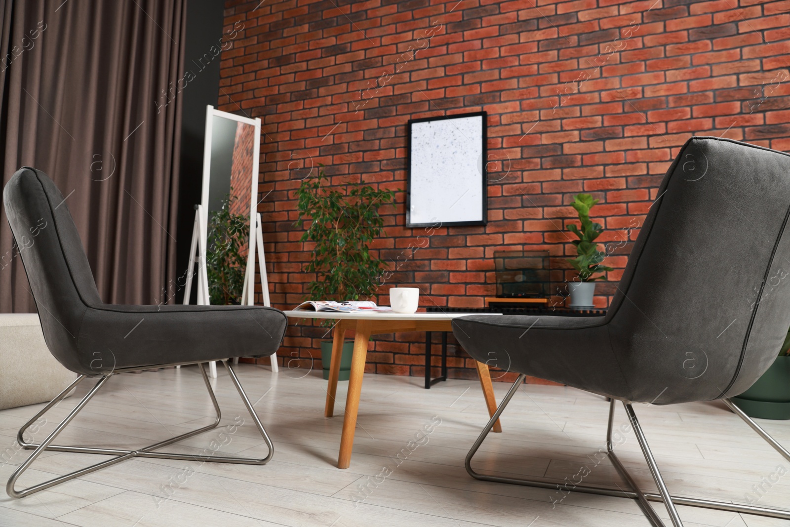 Photo of Soft armchairs, coffee table, mirror and houseplants in cozy living room, low angle view. Interior design