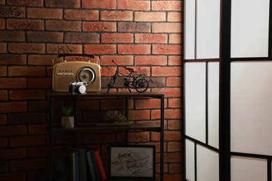 Photo of Shelving unit with different decor, radio receiver and camera near brick wall