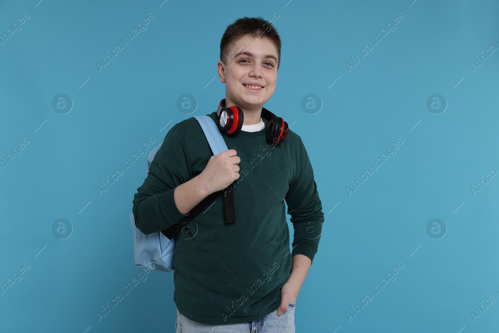 Photo of Teenage boy with backpack and headphones on light blue background