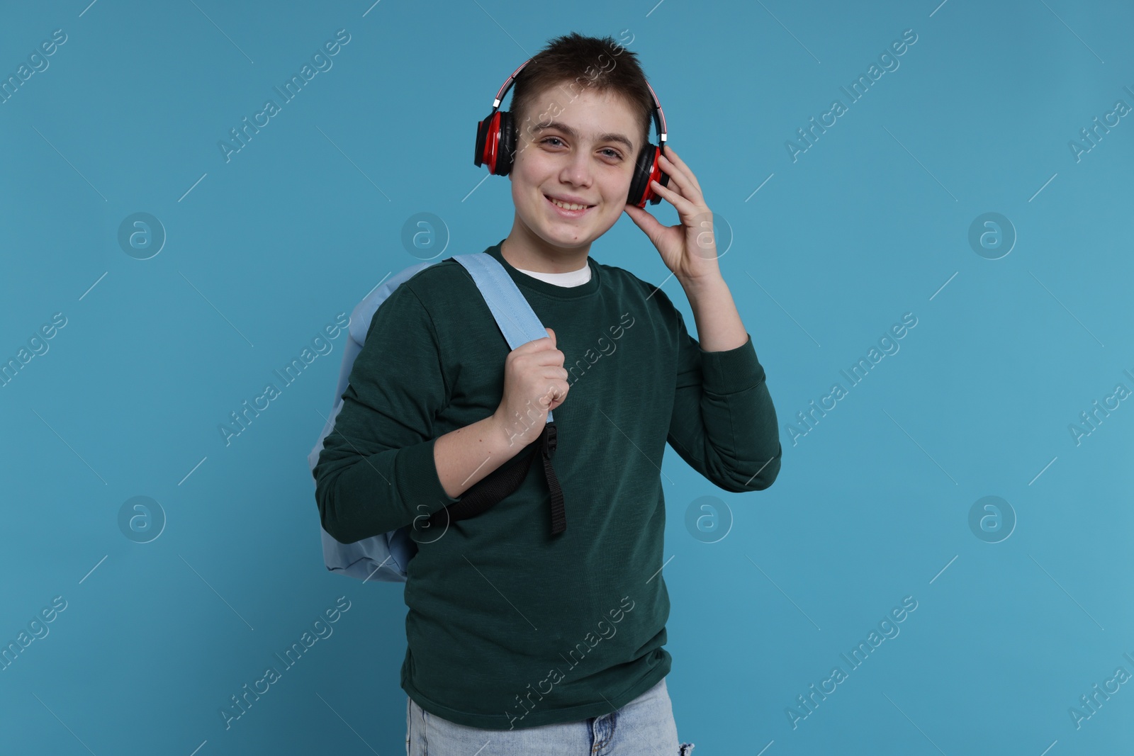 Photo of Teenage boy with backpack and headphones on light blue background