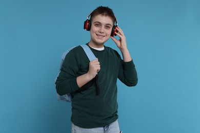 Teenage boy with backpack and headphones on light blue background