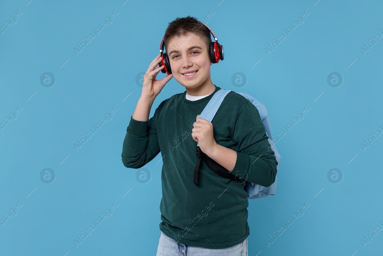 Photo of Teenage boy with backpack and headphones on light blue background