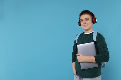 Teenage boy with backpack, headphones and laptop on light blue background, space for text