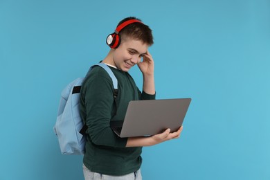 Teenage boy with backpack, headphones and laptop on light blue background