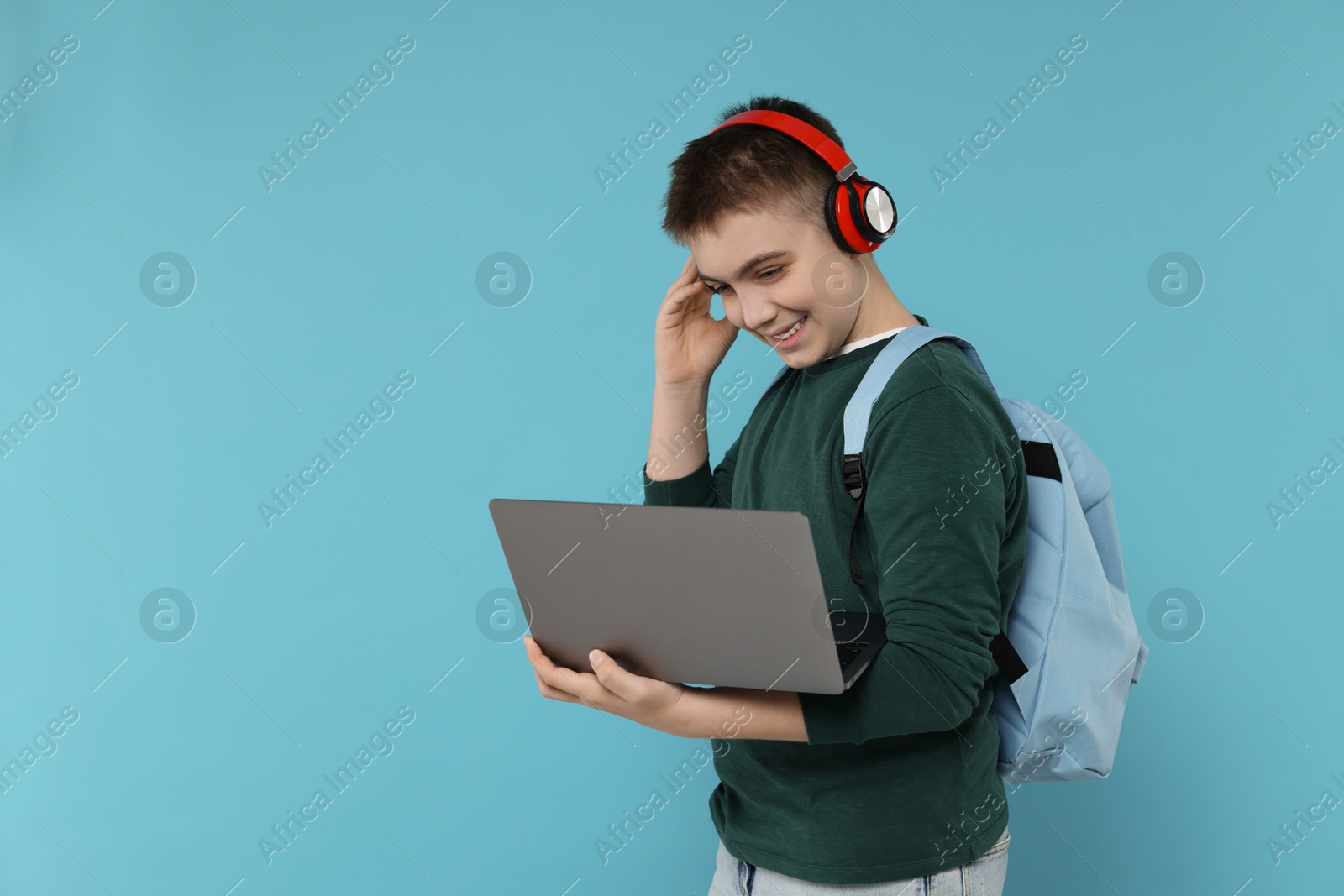 Photo of Teenage boy with backpack, headphones and laptop on light blue background, space for text