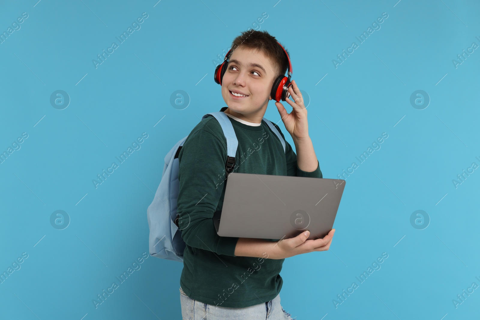 Photo of Teenage boy with backpack, headphones and laptop on light blue background