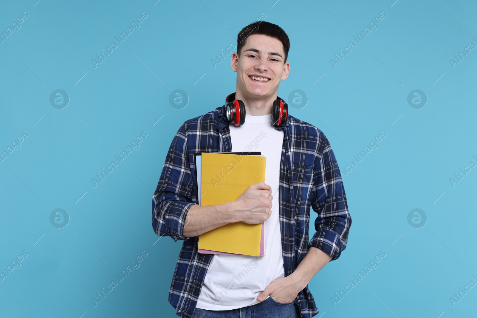 Photo of Student with notebooks and headphones on light blue background