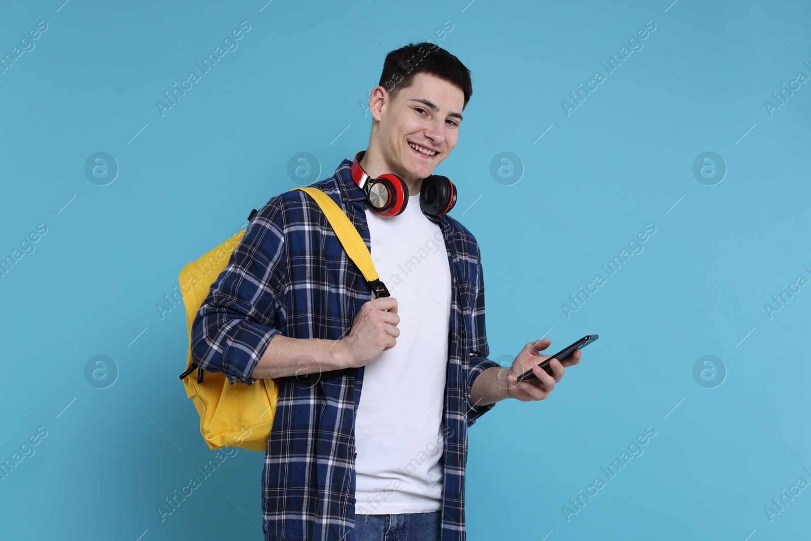 Photo of Student with backpack, smartphone and headphones on light blue background