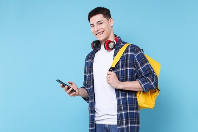 Photo of Student with backpack, smartphone and headphones on light blue background