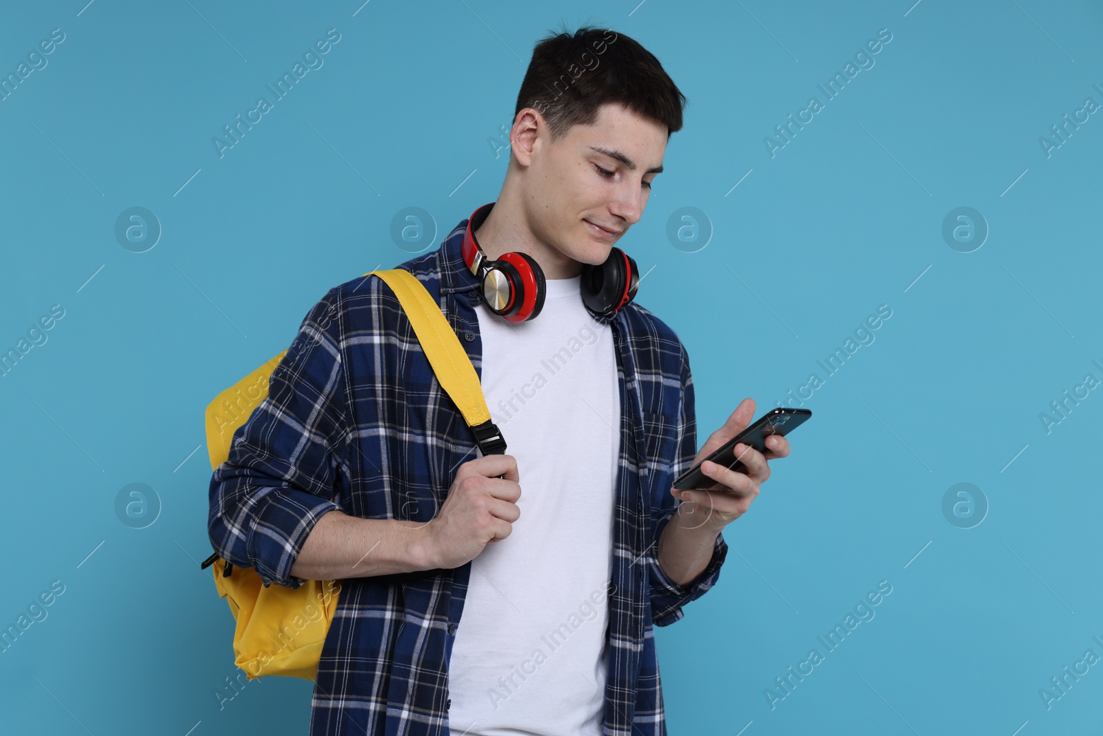 Photo of Student with backpack, smartphone and headphones on light blue background