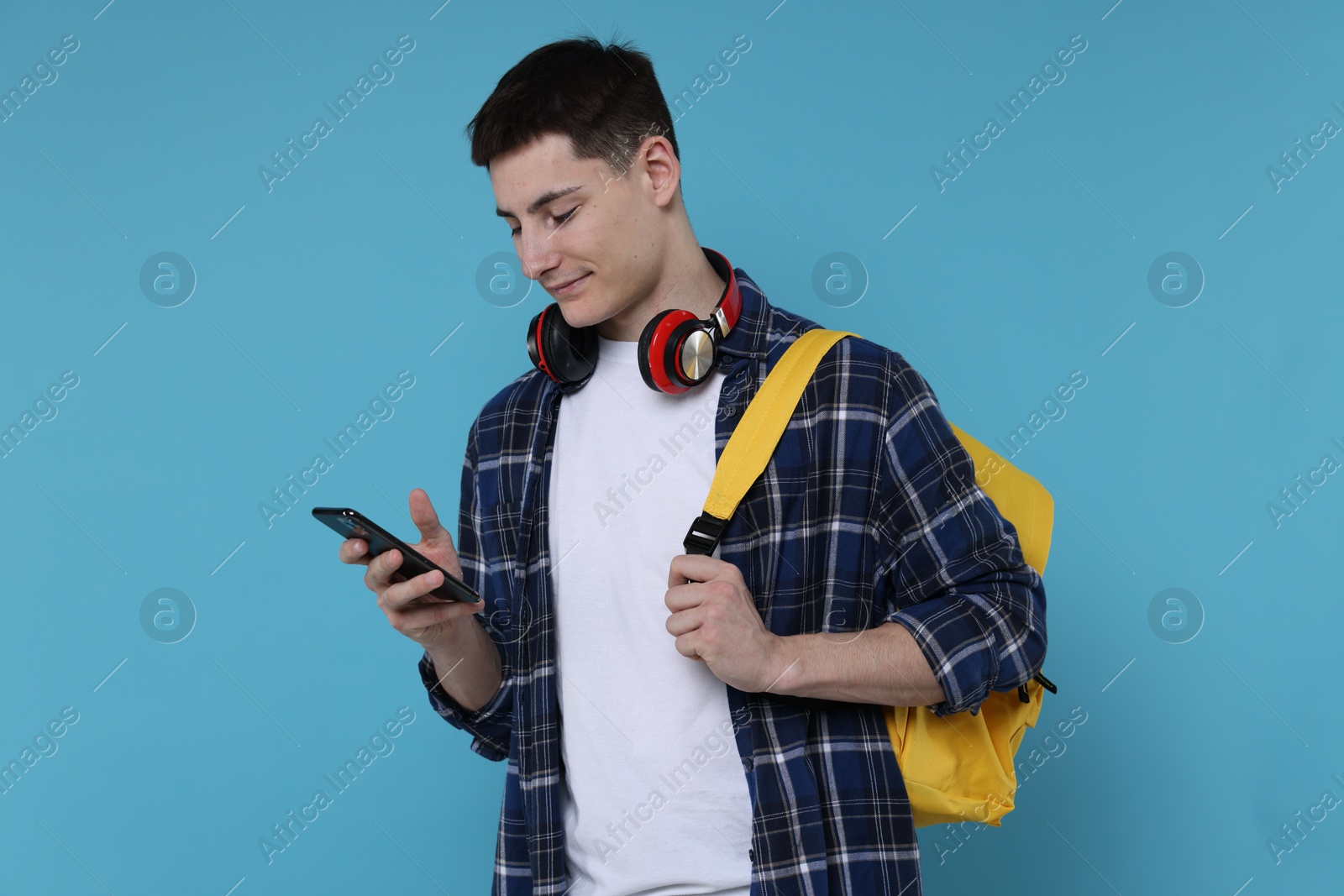 Photo of Student with backpack, smartphone and headphones on light blue background