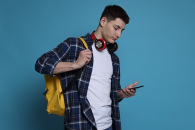 Photo of Student with backpack, smartphone and headphones on light blue background