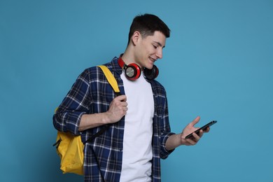 Student with backpack, smartphone and headphones on light blue background