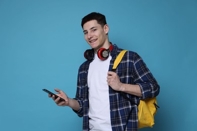 Photo of Student with backpack, smartphone and headphones on light blue background