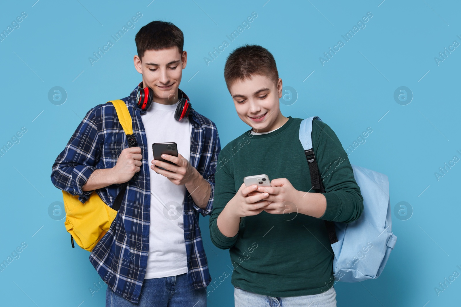 Photo of Students with smartphones and backpacks on light blue background