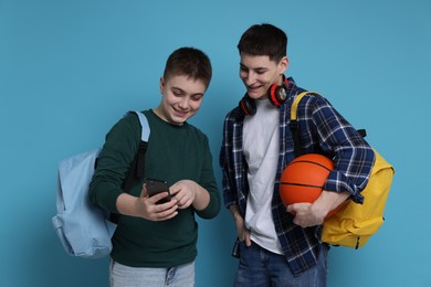 Photo of Teenage boy showing something on smartphone to his friend against light blue background