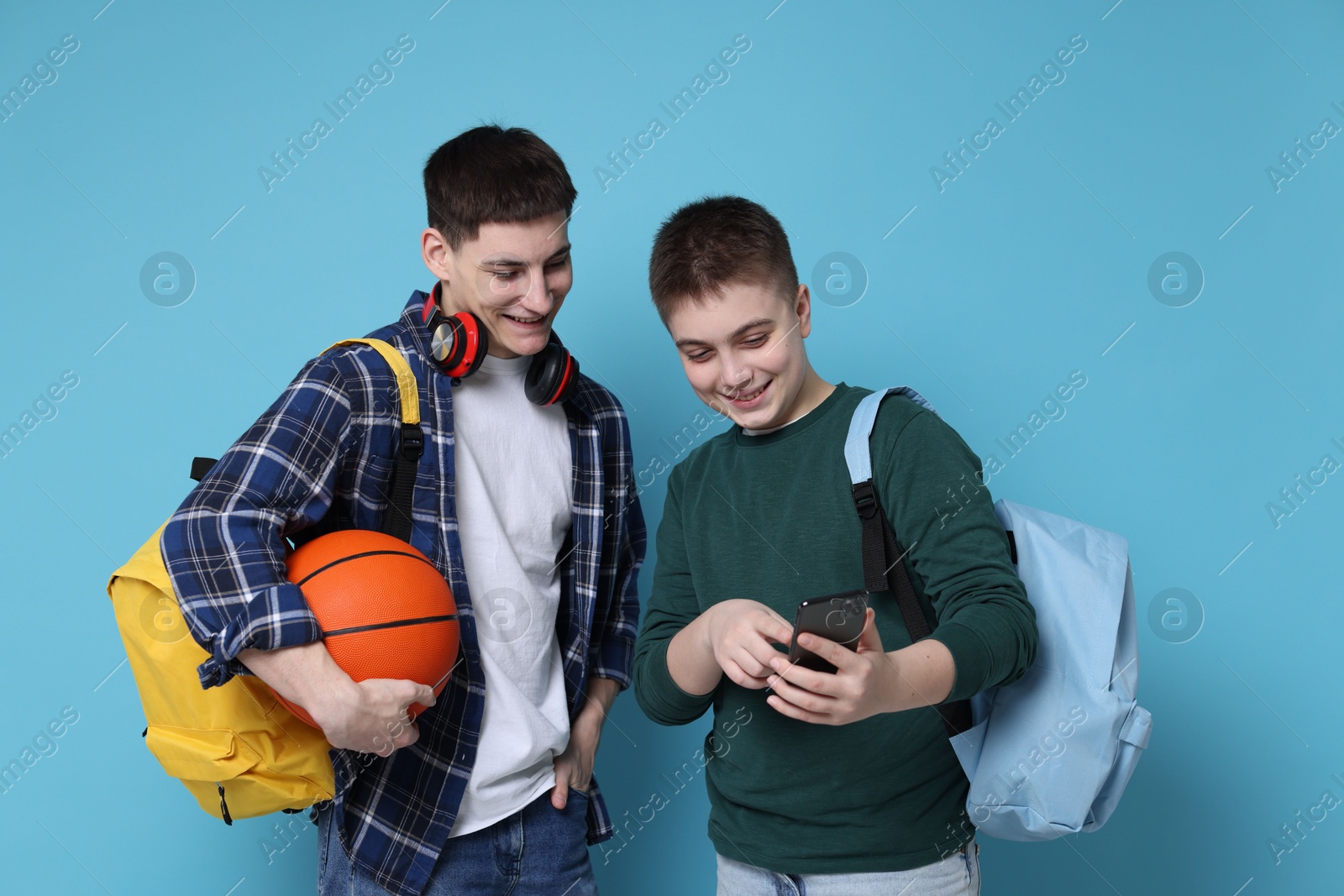 Photo of Teenage boy showing something on smartphone to his friend against light blue background