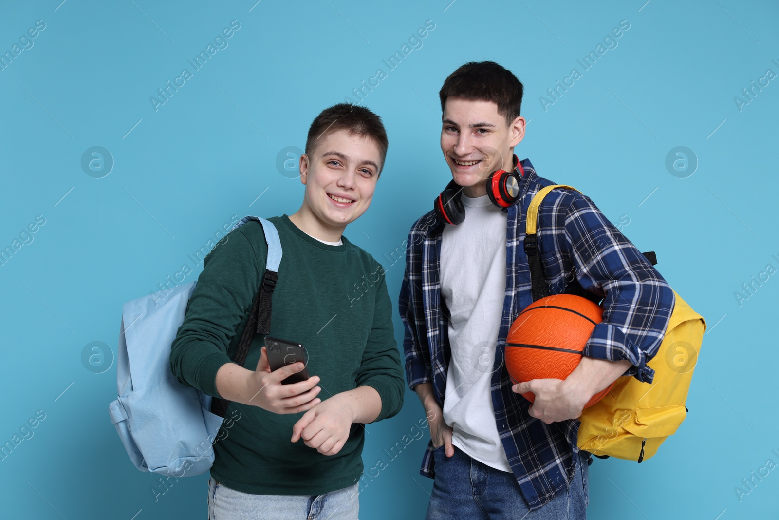 Photo of Students with backpacks, smartphone and basketball ball on light blue background