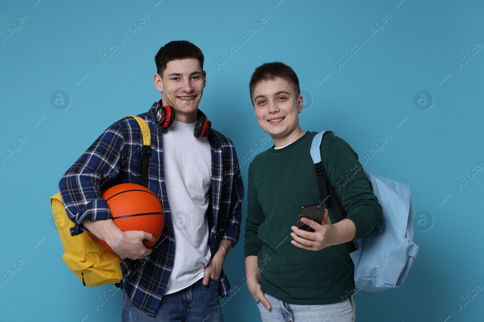 Photo of Students with backpacks, smartphone and basketball ball on light blue background