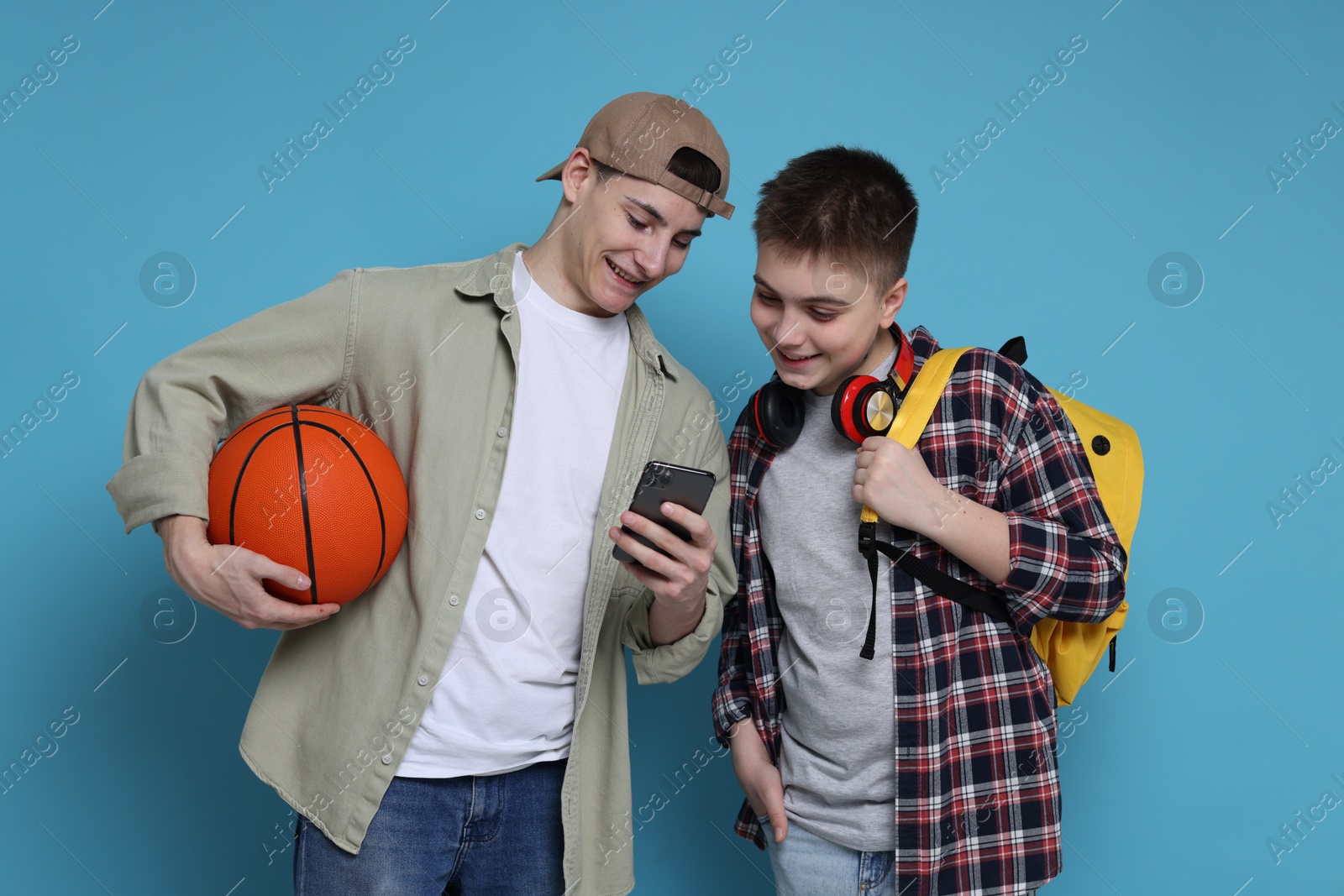 Photo of Student showing something on smartphone to his friend against light blue background