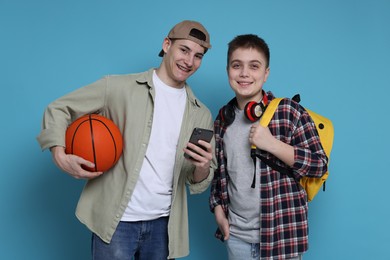 Photo of Students with backpacks, smartphone and basketball ball on light blue background