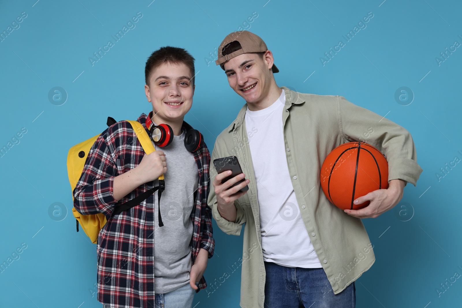 Photo of Students with backpacks, smartphone and basketball ball on light blue background