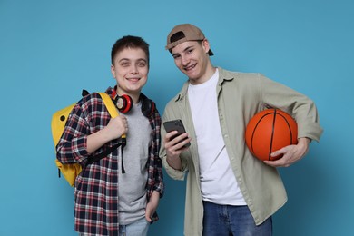 Students with backpacks, smartphone and basketball ball on light blue background