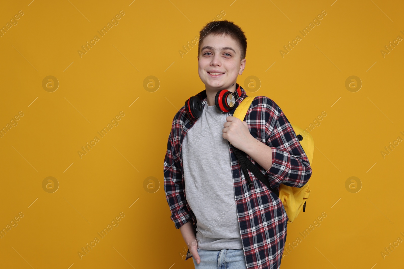 Photo of Teenage boy with headphones and backpack on orange background