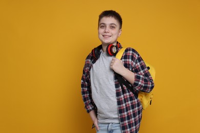 Teenage boy with headphones and backpack on orange background