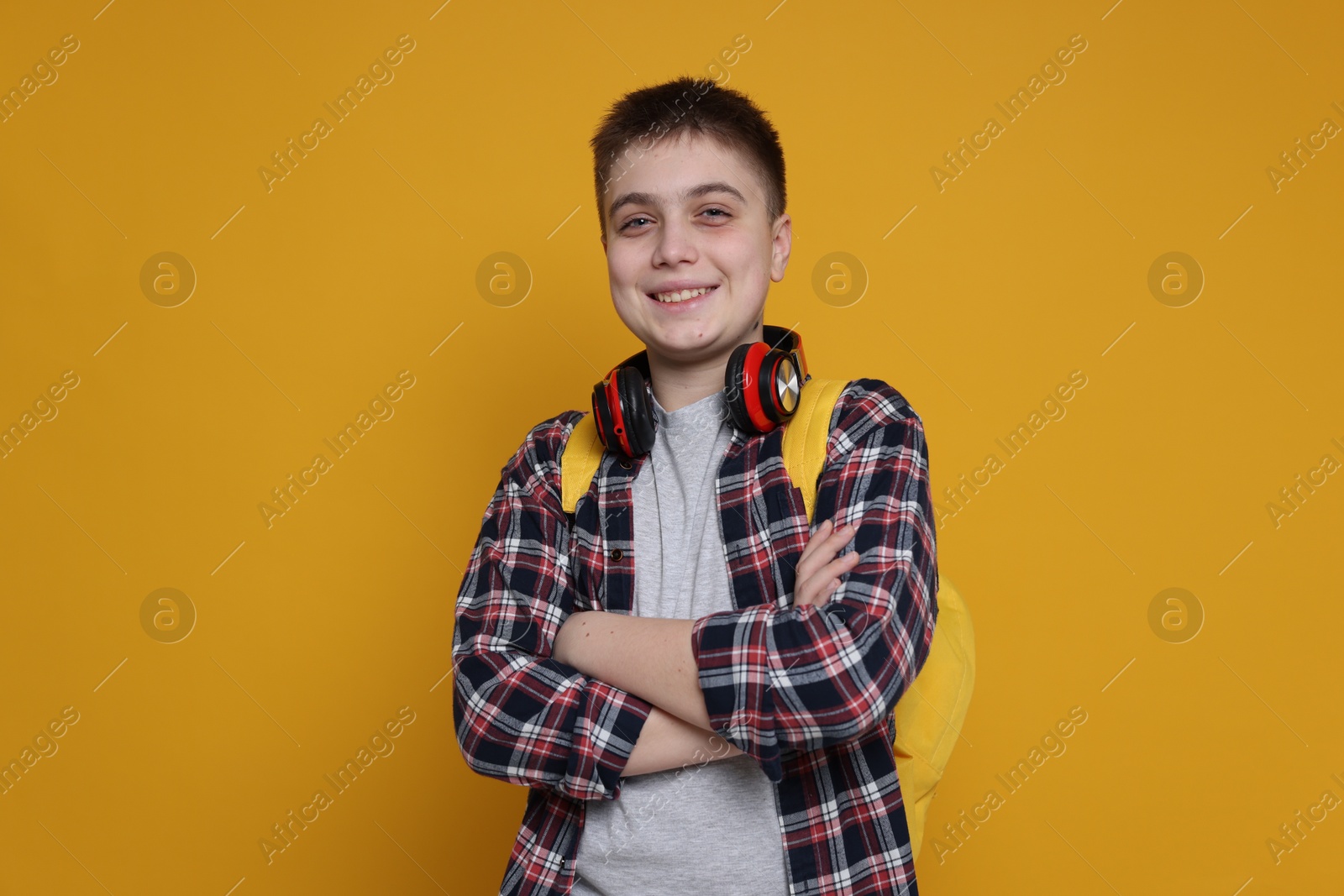 Photo of Teenage boy with headphones and backpack on orange background