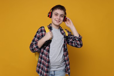 Photo of Teenage boy with headphones and backpack on orange background