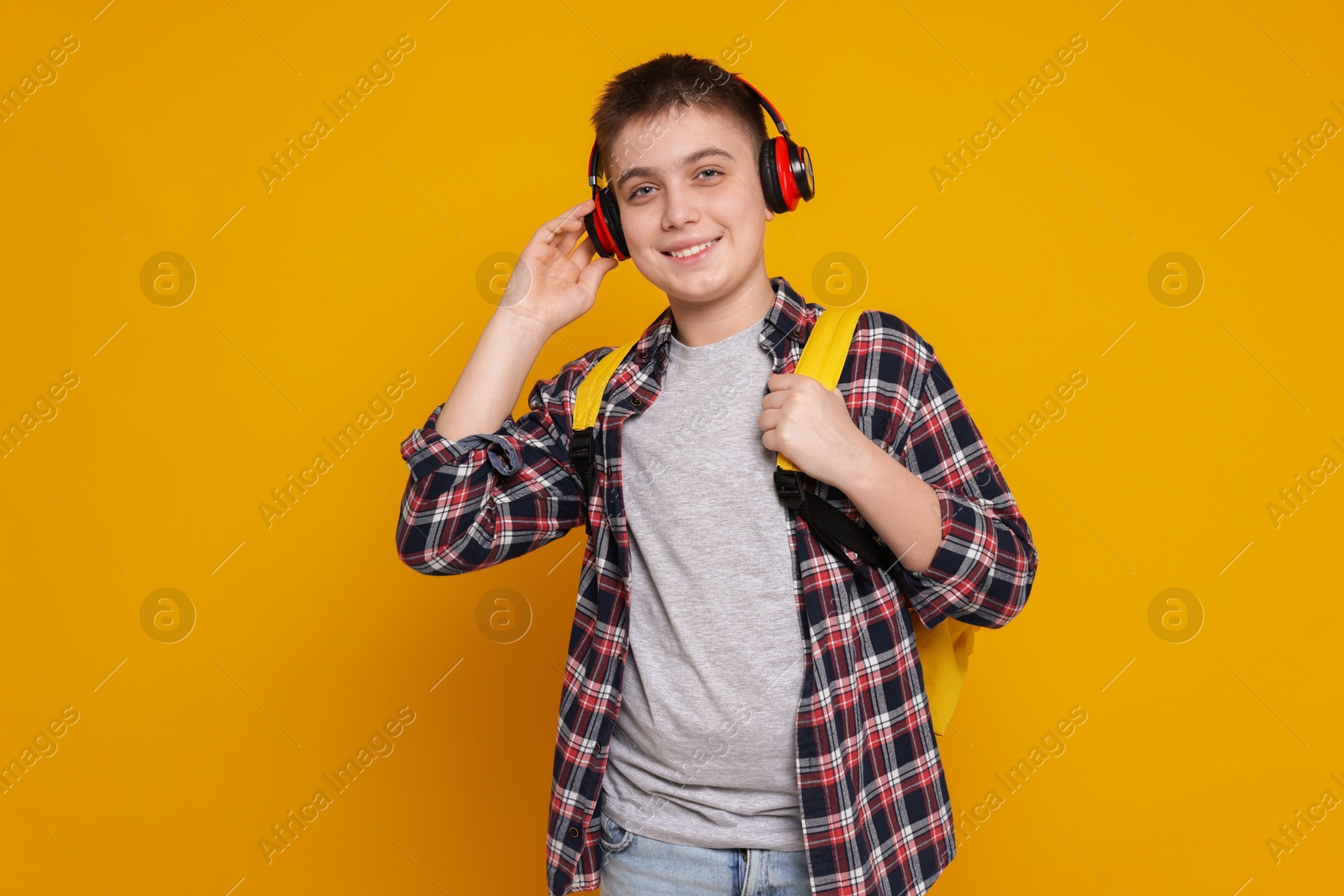 Photo of Teenage boy with headphones and backpack on orange background