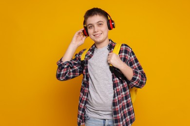 Photo of Teenage boy with headphones and backpack on orange background