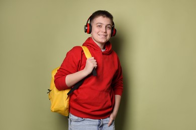 Teenage boy with headphones and backpack on olive background