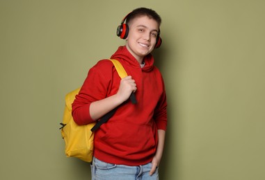 Photo of Teenage boy with headphones and backpack on olive background