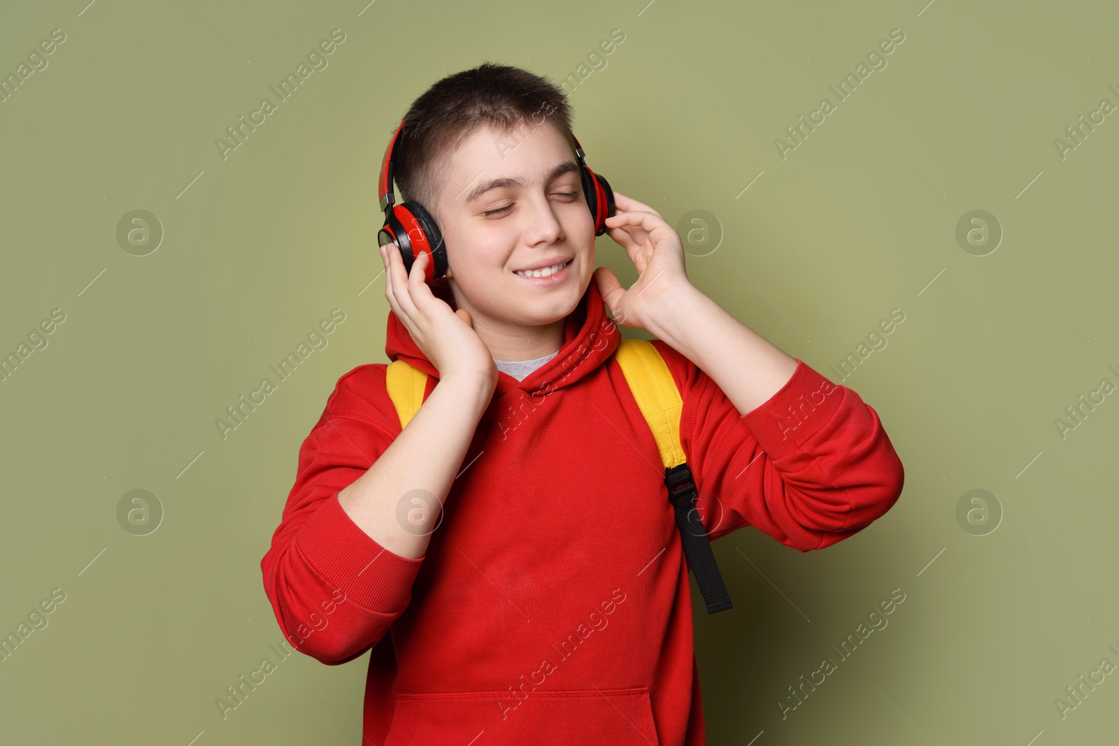 Photo of Teenage boy with headphones and backpack on olive background