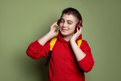 Photo of Teenage boy with headphones and backpack on olive background