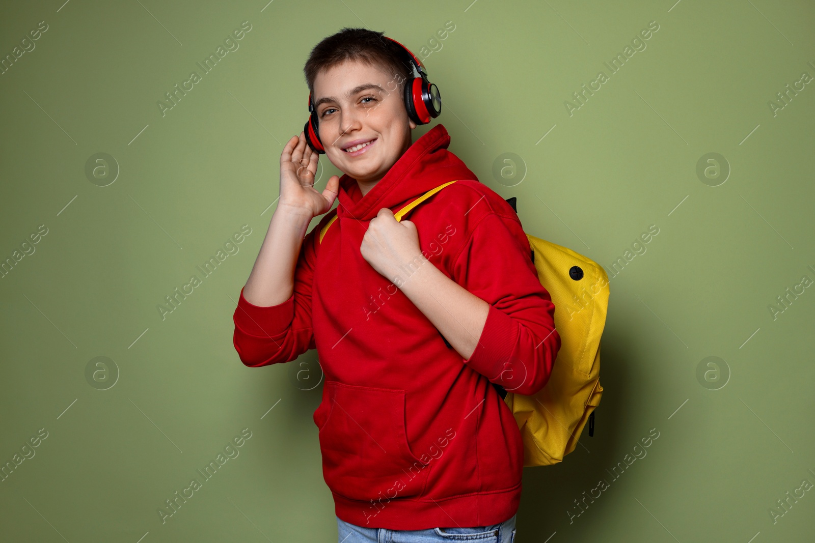 Photo of Teenage boy with headphones and backpack on olive background