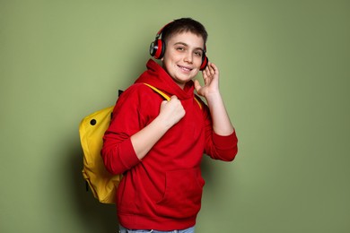 Photo of Teenage boy with headphones and backpack on olive background