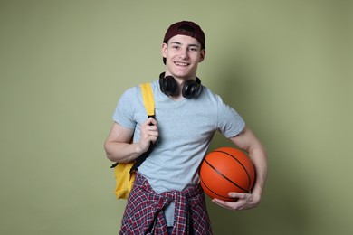 Student with headphones, basketball ball and backpack on olive background