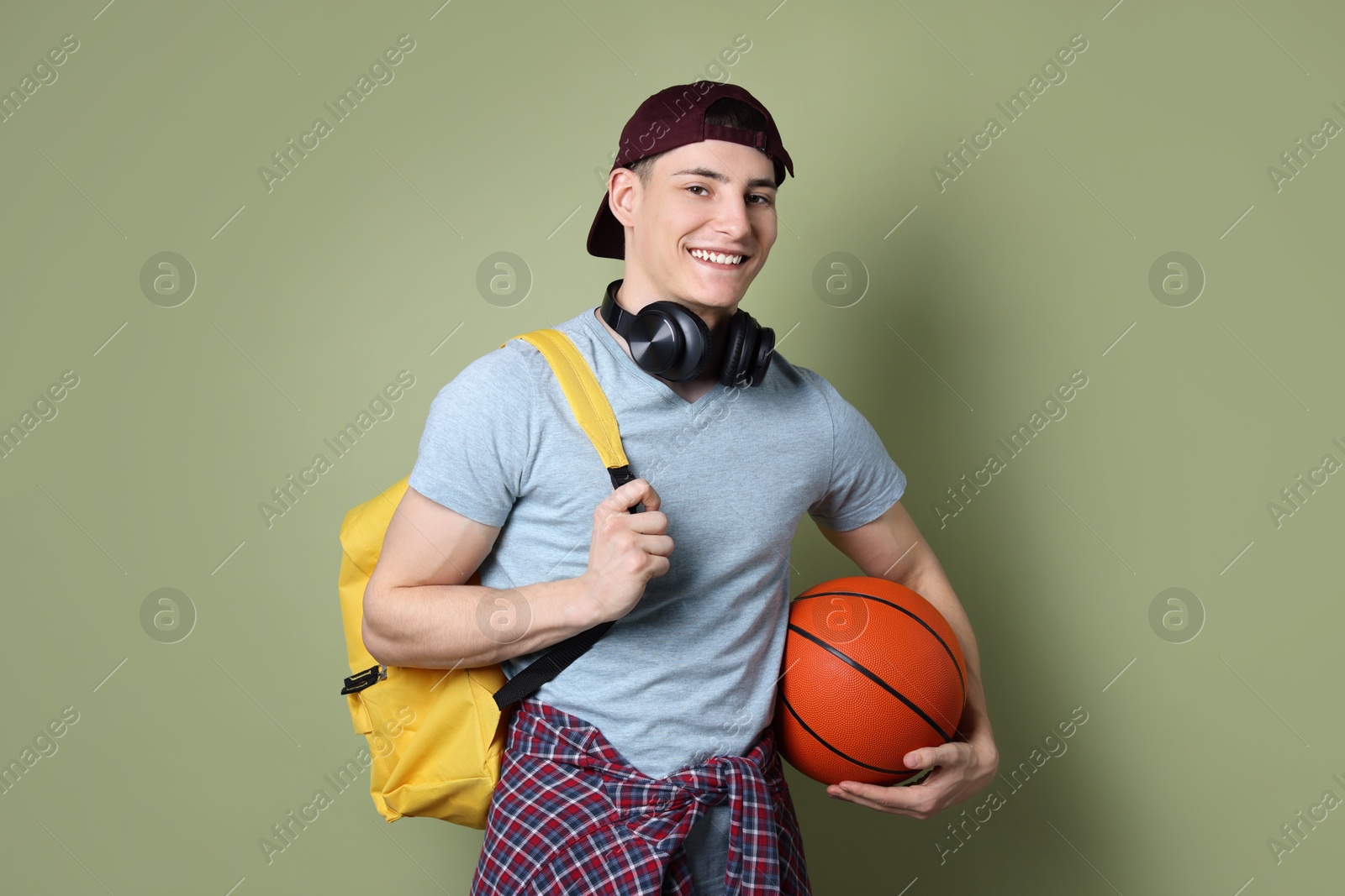 Photo of Student with headphones, basketball ball and backpack on olive background