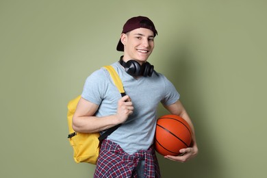 Student with headphones, basketball ball and backpack on olive background