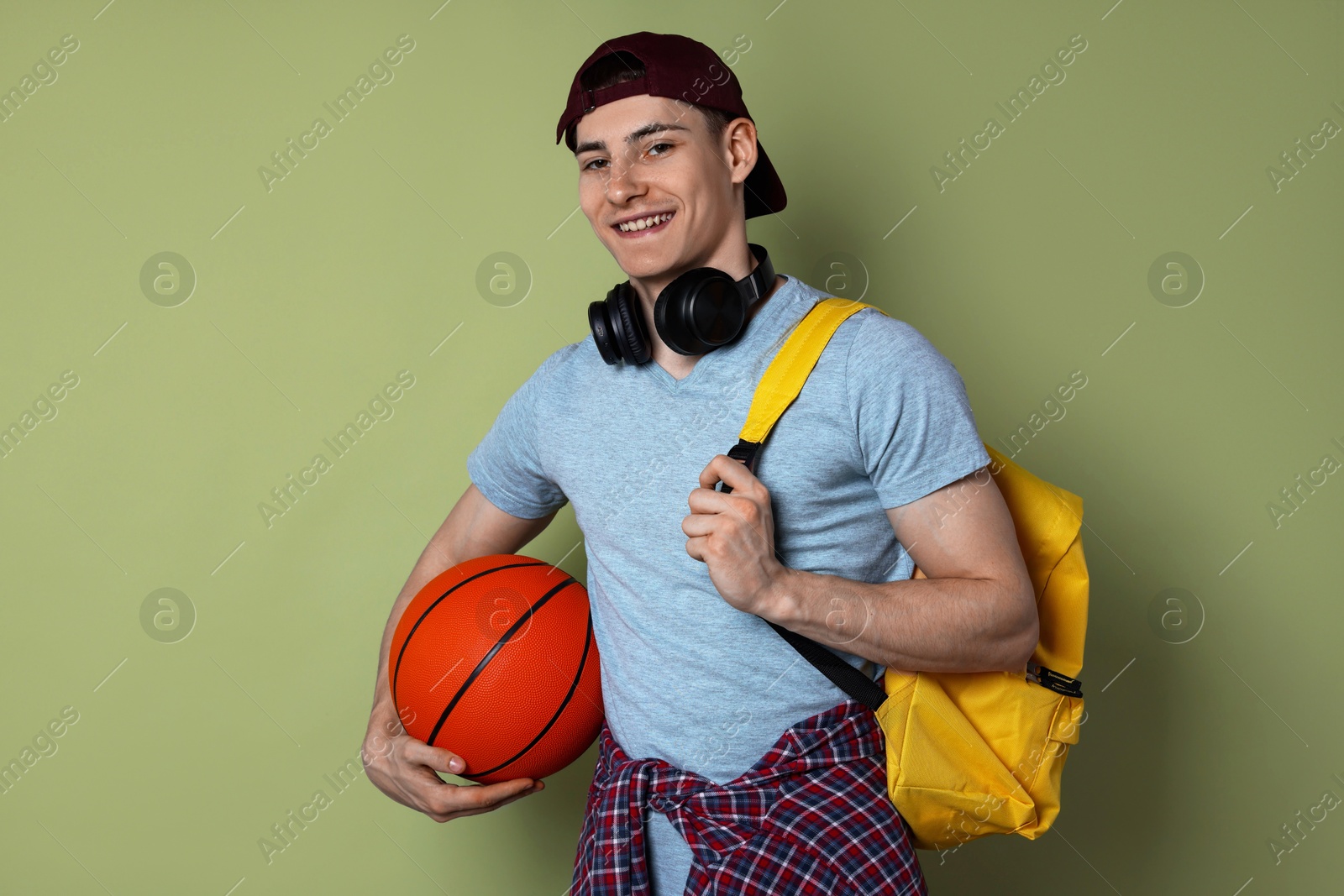 Photo of Student with headphones, basketball ball and backpack on olive background