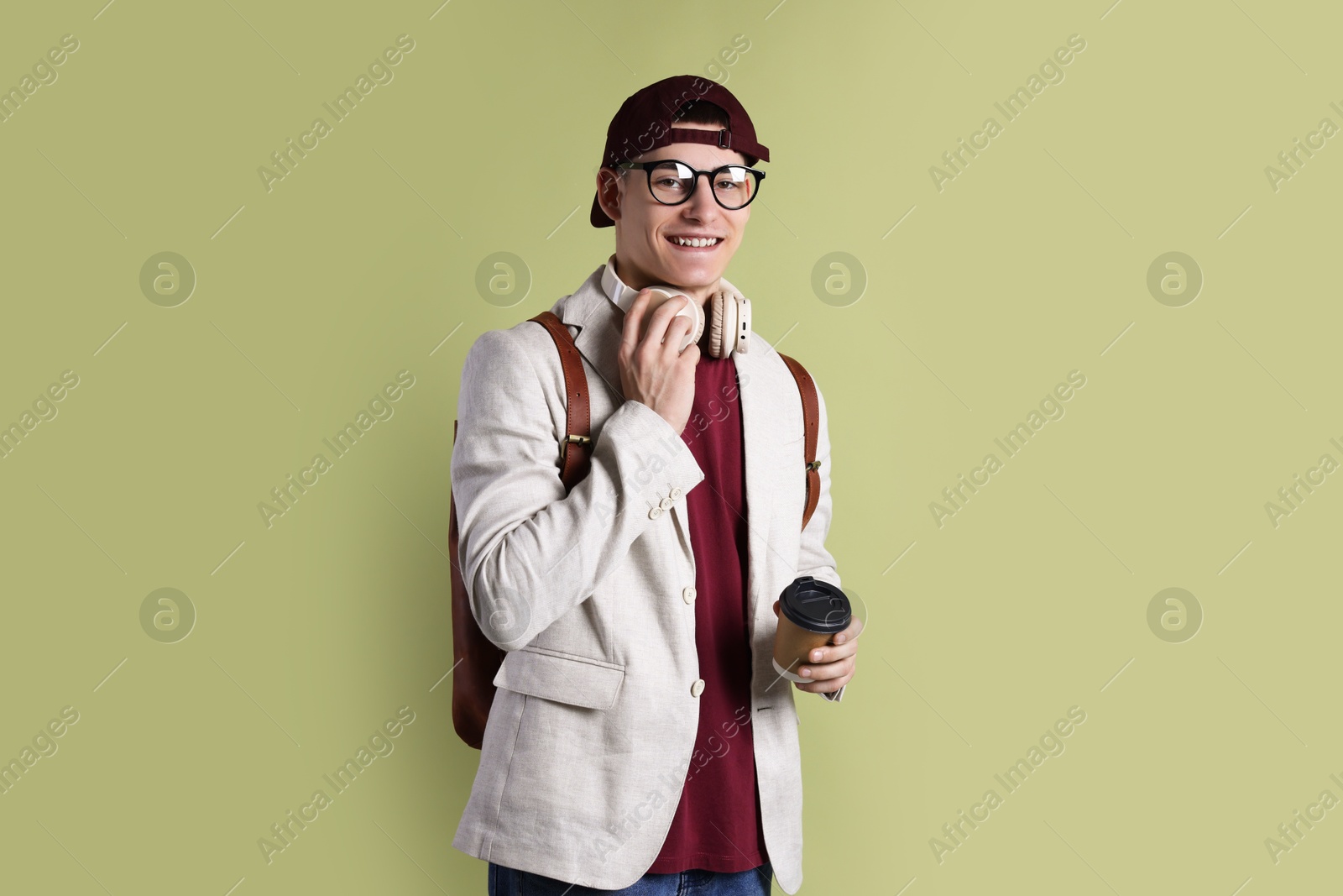 Photo of Student with headphones, paper cup of coffee and backpack on olive background