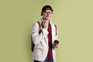 Photo of Student with headphones, paper cup of coffee and backpack on olive background