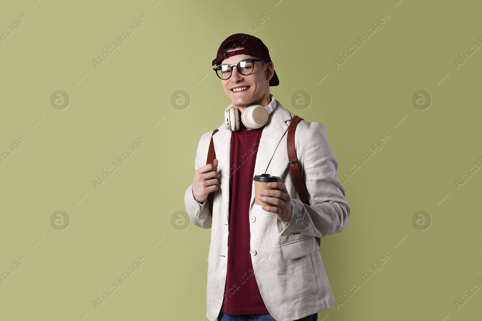 Photo of Student with headphones, paper cup of coffee and backpack on olive background