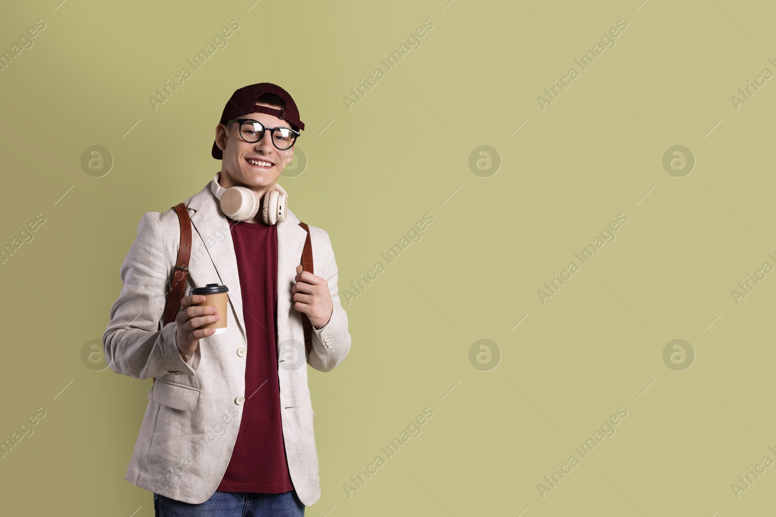 Photo of Student with headphones, paper cup of coffee and backpack on olive background, space for text