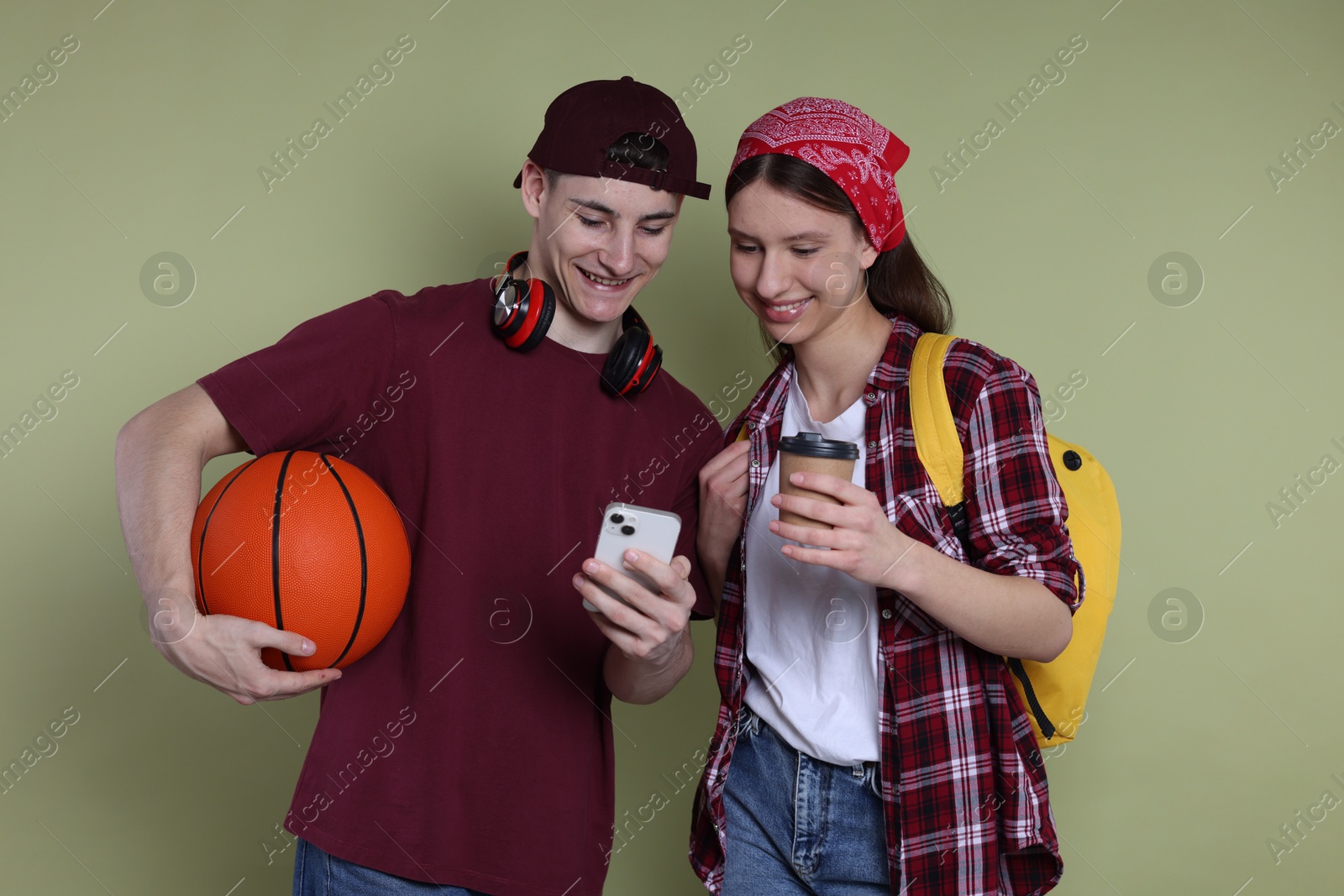 Photo of Student showing something on smartphone to girl against olive background