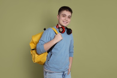 Teenage boy with headphones and backpack on olive background